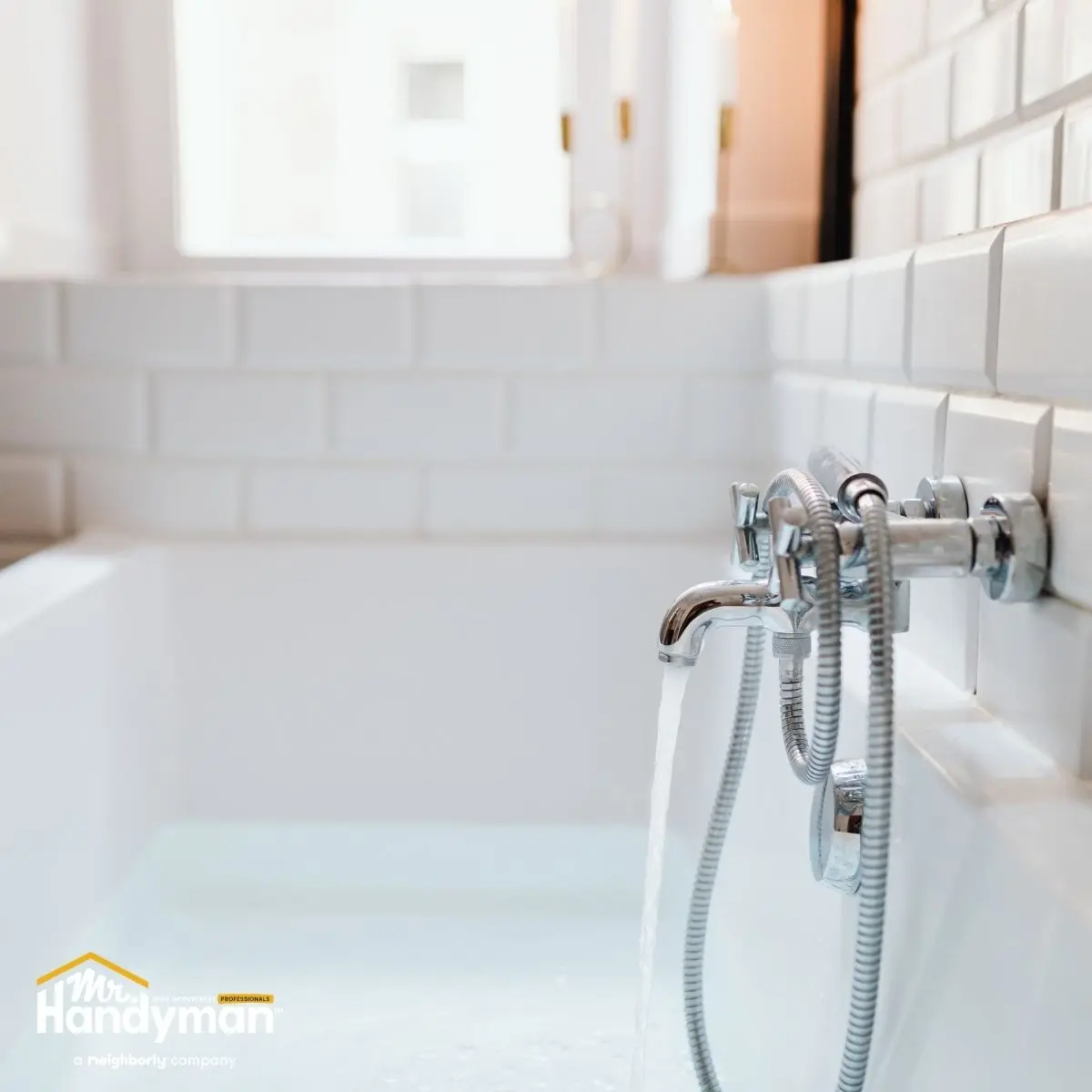 A chrome bathtub faucet with a handheld shower hose is running water into a white bathtub