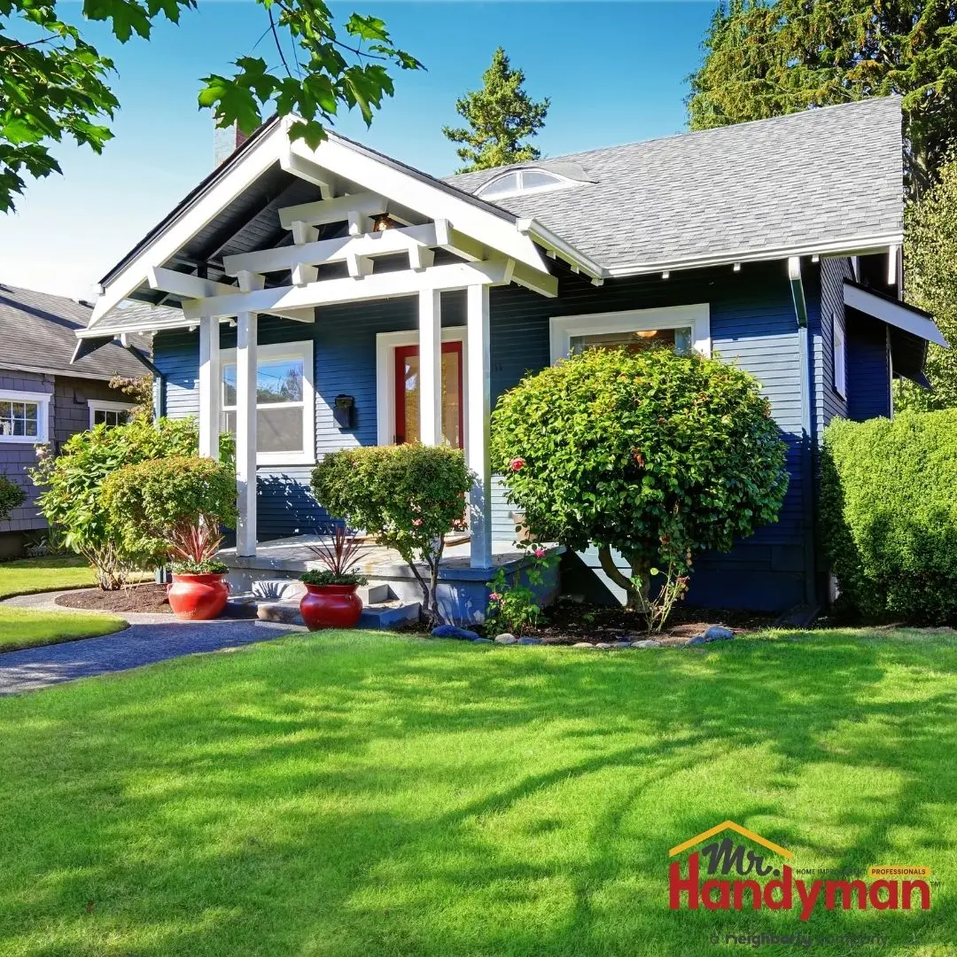 A blue house with white trim, featuring a well-kept front yard with manicured bushes and potted plants.