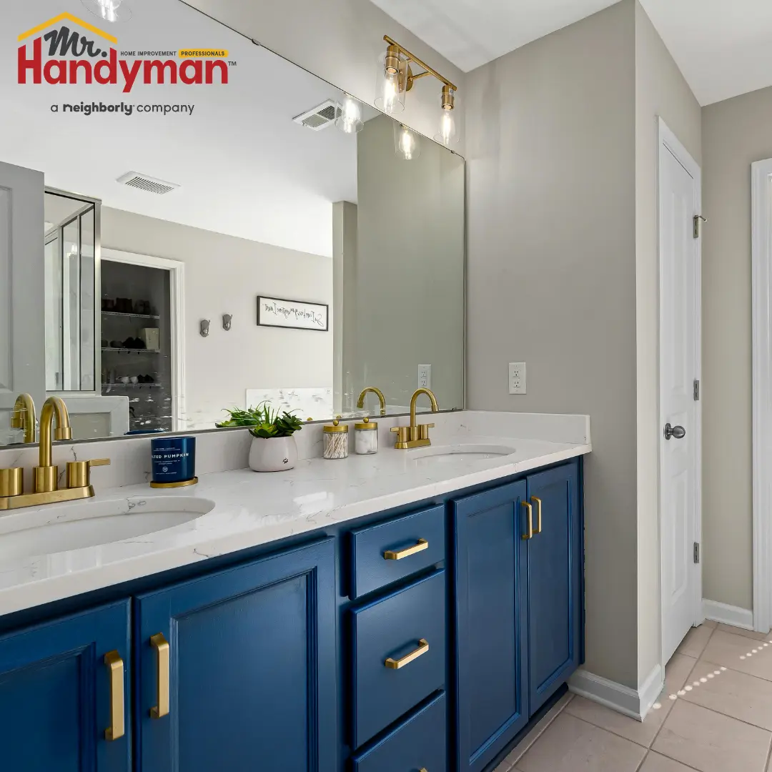A bathroom vanity features blue cabinets, gold faucets and a large mirror.