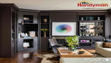A modern living room featuring custom, dark-painted built-in cabinetry and a home bar setup.