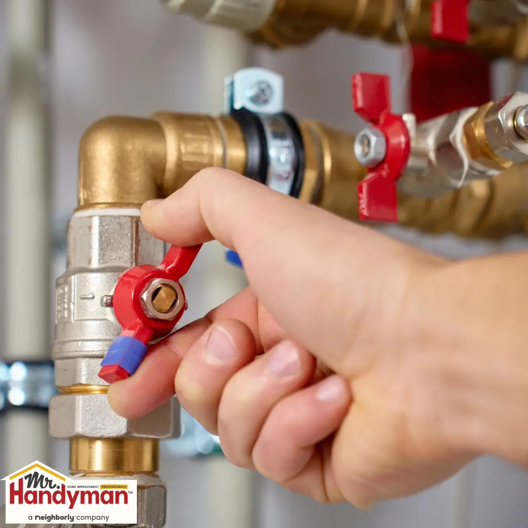 Hand turning red valve on brass plumbing pipe.