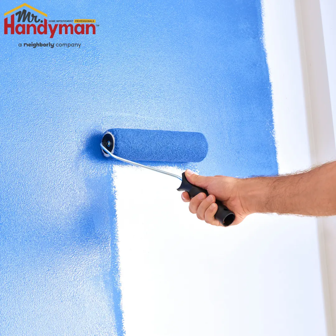 A person painting a wall with a blue roller.