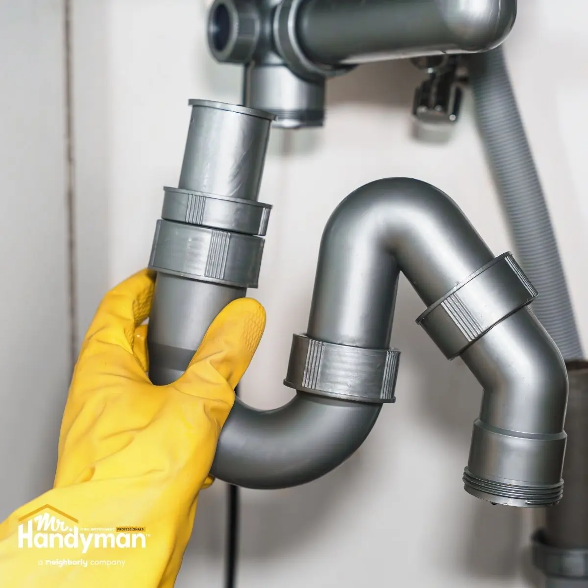 A person is tightening a gray PVC pipe under a sink.