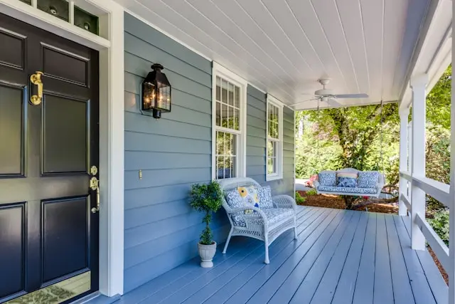 A covered front porch of someone's home with siding that has been freshly cleaned. It is painted blue, and the front door, a bench, and a porch swing are also visible.