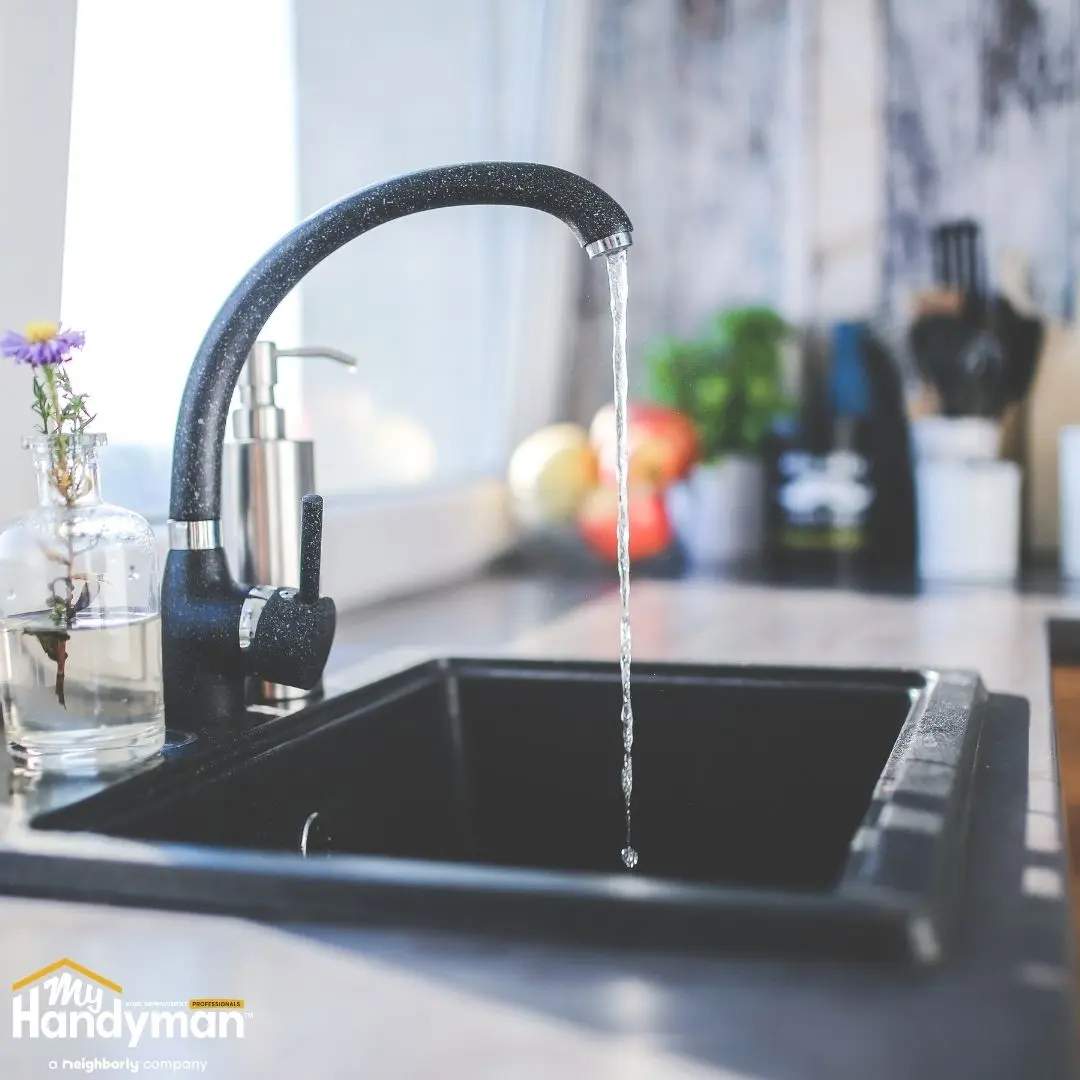 A modern kitchen sink with a sleek black faucet, water flowing.
