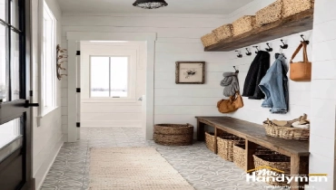 Bright mudroom with white walls, patterned tile floor, wooden bench with baskets, and wall hooks for coats and bags.