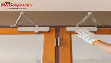 Mr. Handyman technician repairing entry flooring and door hardware in a high-traffic business.