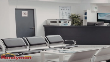 A modern medical clinic waiting area with black leather seating, a reception counter, and informational posters on health topics.