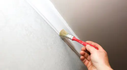 Man painting crown molding with a small paintbrush.