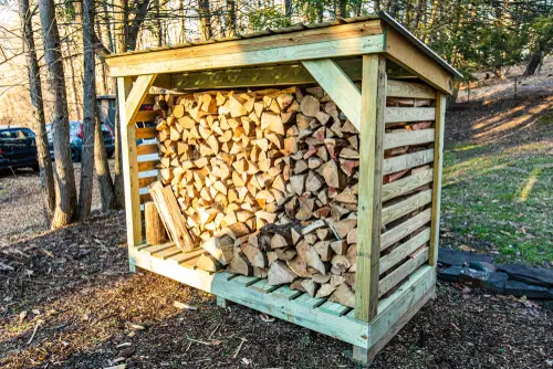 Sturdy DIY firewood rack made from pressure-treated wood and metal connectors, filled with stacked logs and set against an outdoor backdrop.