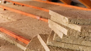 Batts of mineral wool attic insulation stacked together and laid out across the floor of a residential attic.