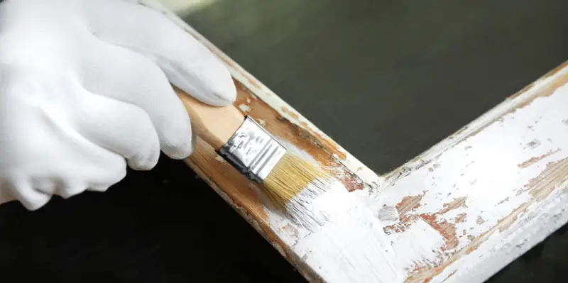 A handyman painting part of a home&rsquo;s exterior trim during an appointment for trim repair.