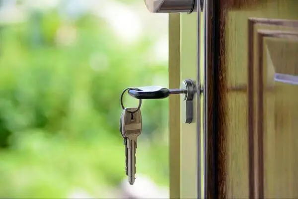 A set of keys in a door lock. The door is partially open to the outside.