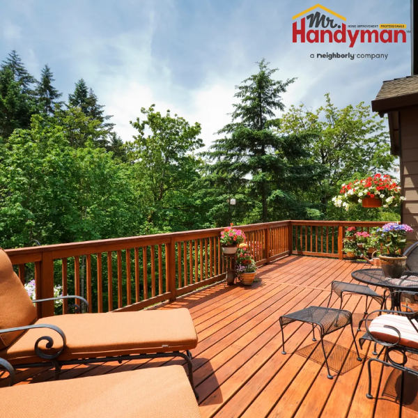 A sunny wooden deck with a pergola, a bench, a small table, and four cushioned chairs in a backyard garden setting.