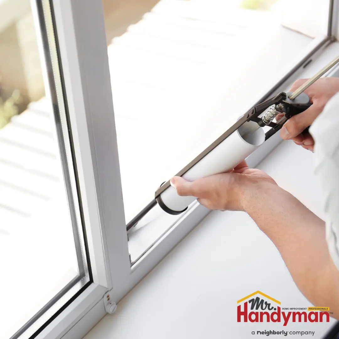 A person applying sealant to the gap between a window frame and the glass using a caulking gun.