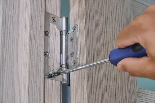 Close-up of a person tightening a door hinge with a screwdriver to fix a sagging door.