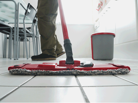 A mop being used to clean the floors in a bright white kitchen.